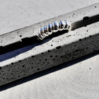 A silver metallic ring with a textured, coiled or segmented design, resting on a speckled gray concrete surface.