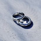 Two polished silver rings with engraved patterns, resting on a textured gray concrete surface under bright natural sunlight.
