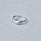 A polished silver ring with an organic, wavy triangular shape, resting on a textured light gray surface.