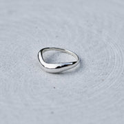 A polished silver ring with an organic, wavy triangular shape, resting on a textured light gray surface.