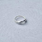 A polished silver ring with a smooth, slightly wavy, teardrop-shaped band, resting on a textured gray surface.