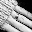 A close-up black and white photo of a hand wearing four slim silver rings.