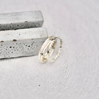 Four silver rings in different textures, displayed on a light gray stone surface next to two textured gray stone bars.