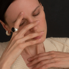 A close-up lifestyle shot of a woman wearing a polished silver signet ring with a black cabochon amber stone on her index finger, paired with a cream knit sweater against a dark background.
