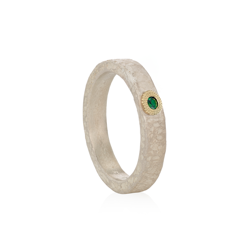 A textured silver ring with a small round green emerald gemstone surrounded by a gold halo, shown on a clean white background.