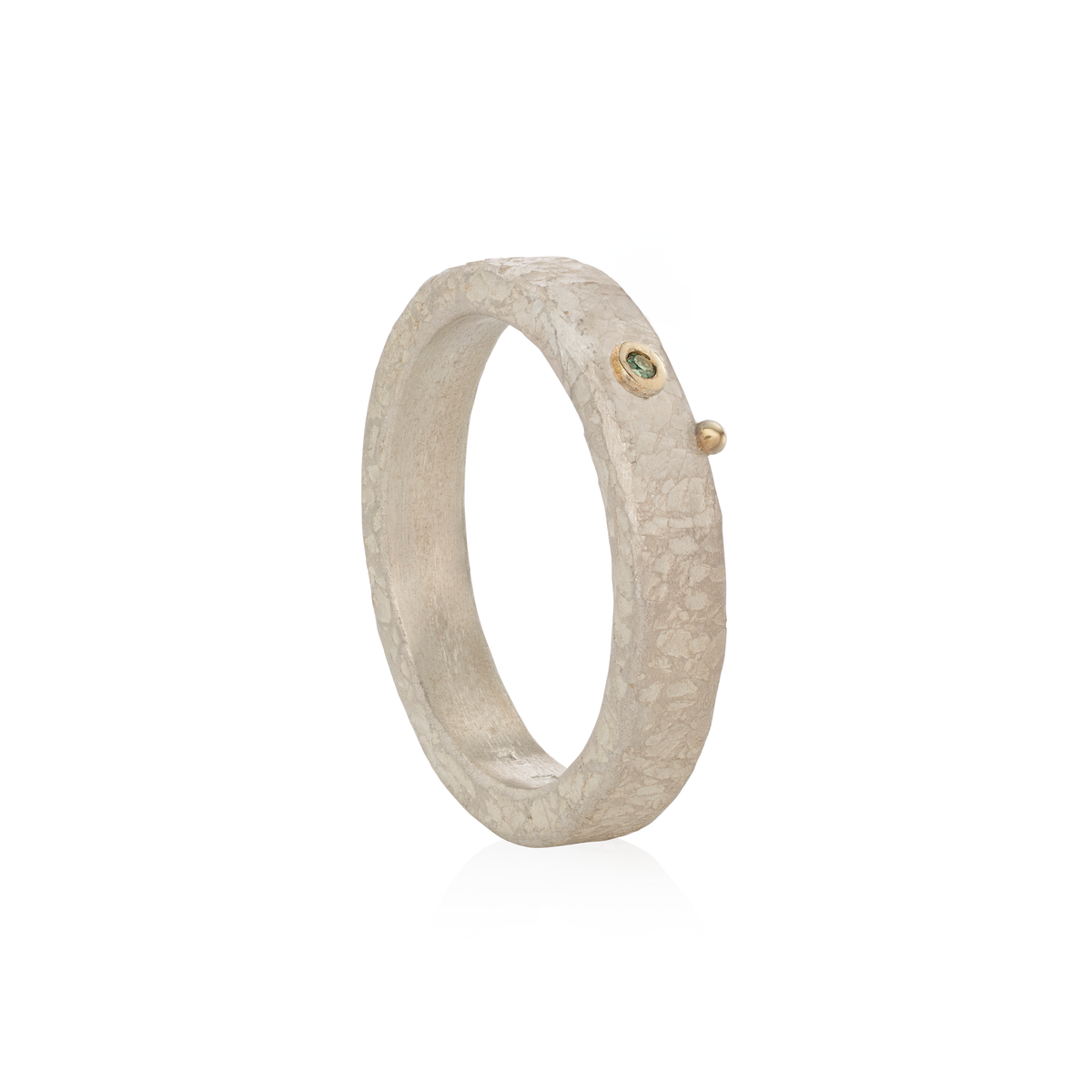 A textured silver band ring with a small gold bezel-set green diamond and a tiny gold accent bead on the side, shown on a clean white background.