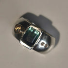 A silver ring featuring a rectangular green iridescent gemstone and two small moissnaites on the band, photographed on a plain light background.