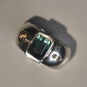 A silver ring featuring a rectangular green iridescent gemstone and two small moissnaites on the band, photographed on a plain light background.