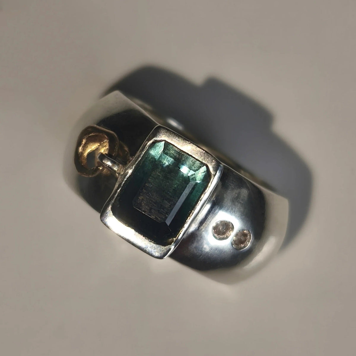 A silver ring featuring a rectangular green iridescent gemstone and two small moissnaites on the band, photographed on a plain light background.