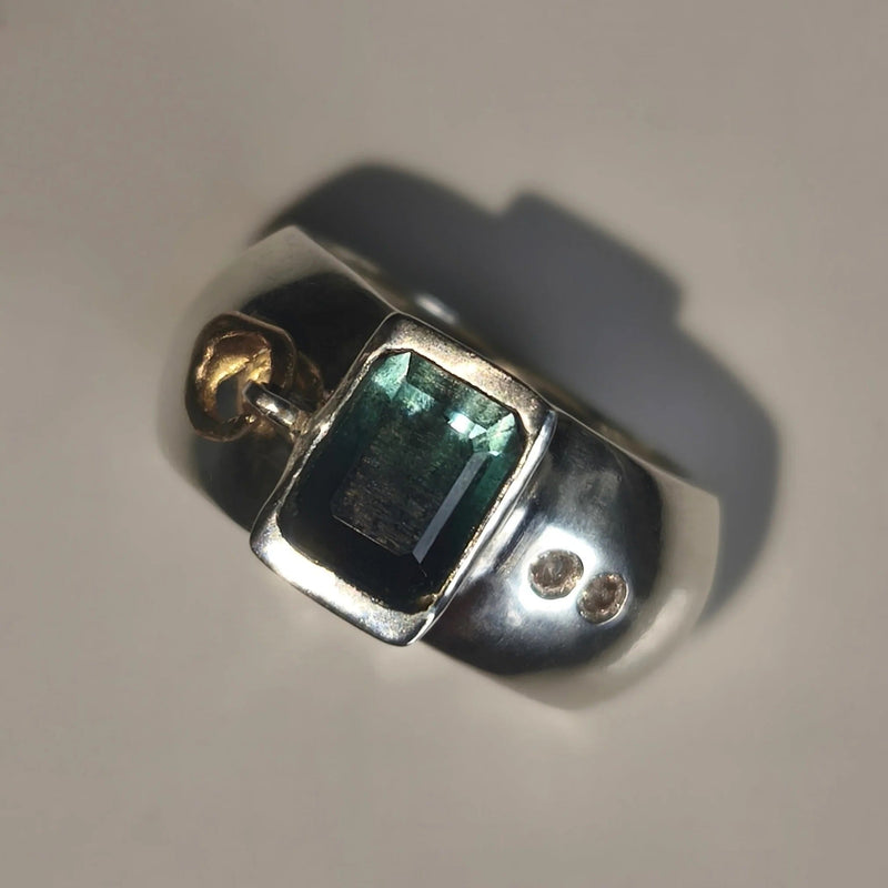 A silver ring featuring a rectangular green iridescent gemstone and two small moissnaites on the band, photographed on a plain light background.