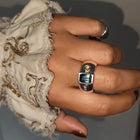 A silver ring featuring a rectangular green iridescent gemstone and two small moissnaites on the band, photographed on a plain light background.