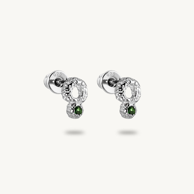A pair of silver stud earrings, featuring a raw, artisanal textured surface and vibrant green emeralds.
