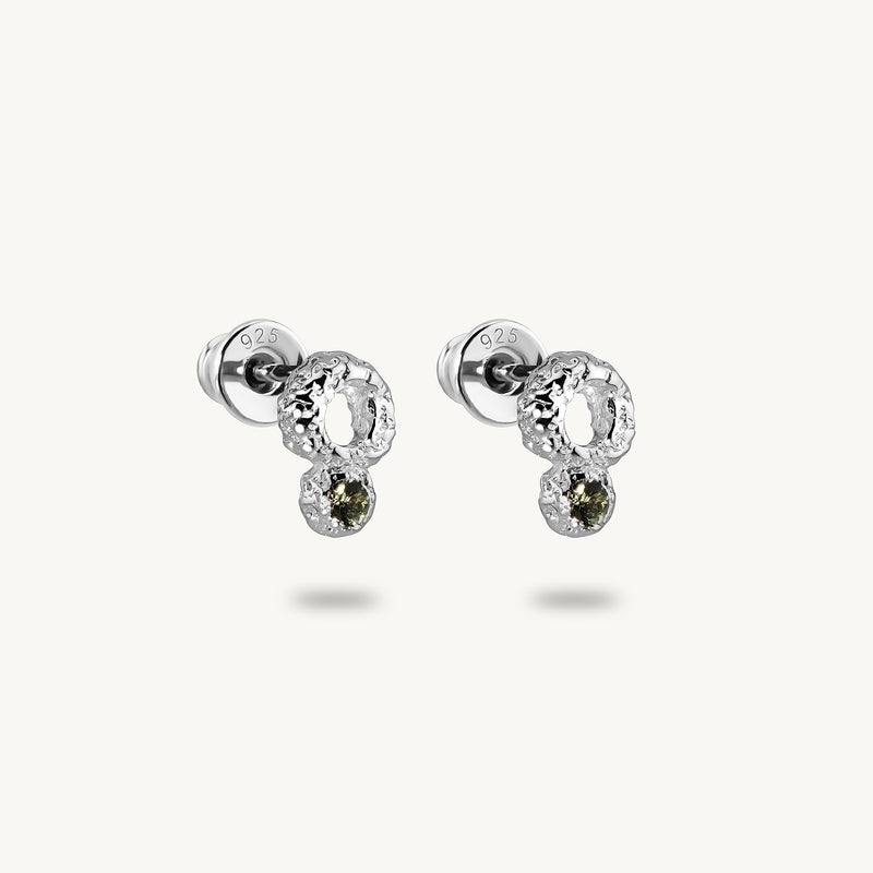 A pair of silver stud earrings with textured circular clusters and small oval green sapphires drops, shown on a light cream background.