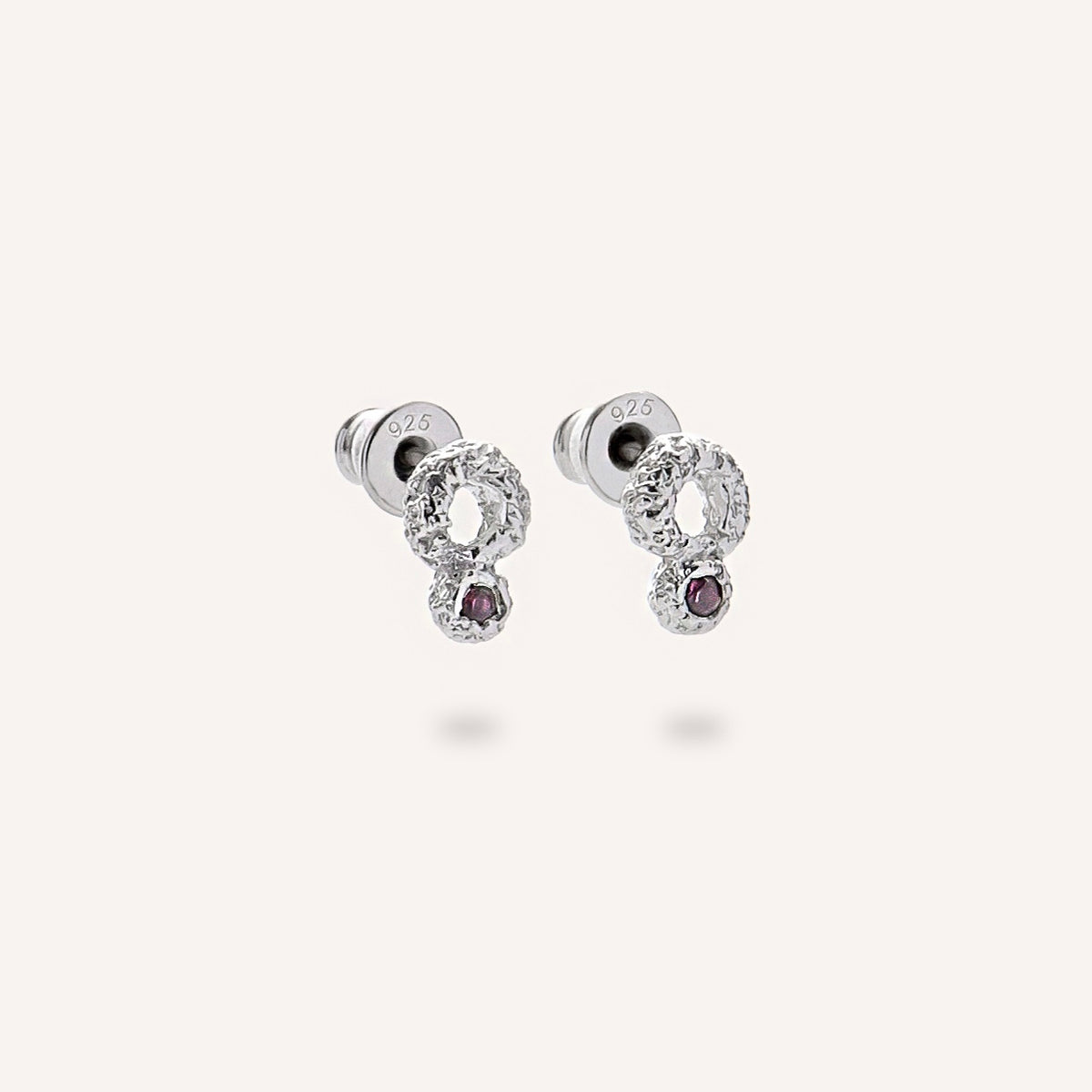 Pair of stud earrings made from silver, featuring a raw, artisanal textured surface and vibrant red sapphires. 