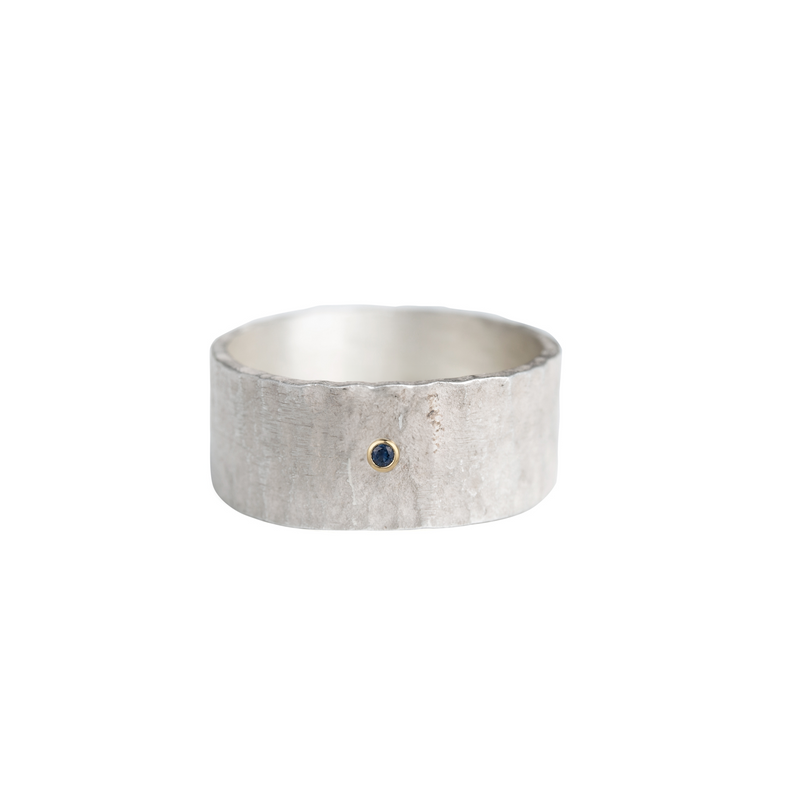A wide sterling silver band with a hammered surface set with a blue diamond. 