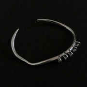 One-of-a-kind silver bangle featuring an organic, asymmetrical shape with delicate dangling accents for a modern, minimalist edge.