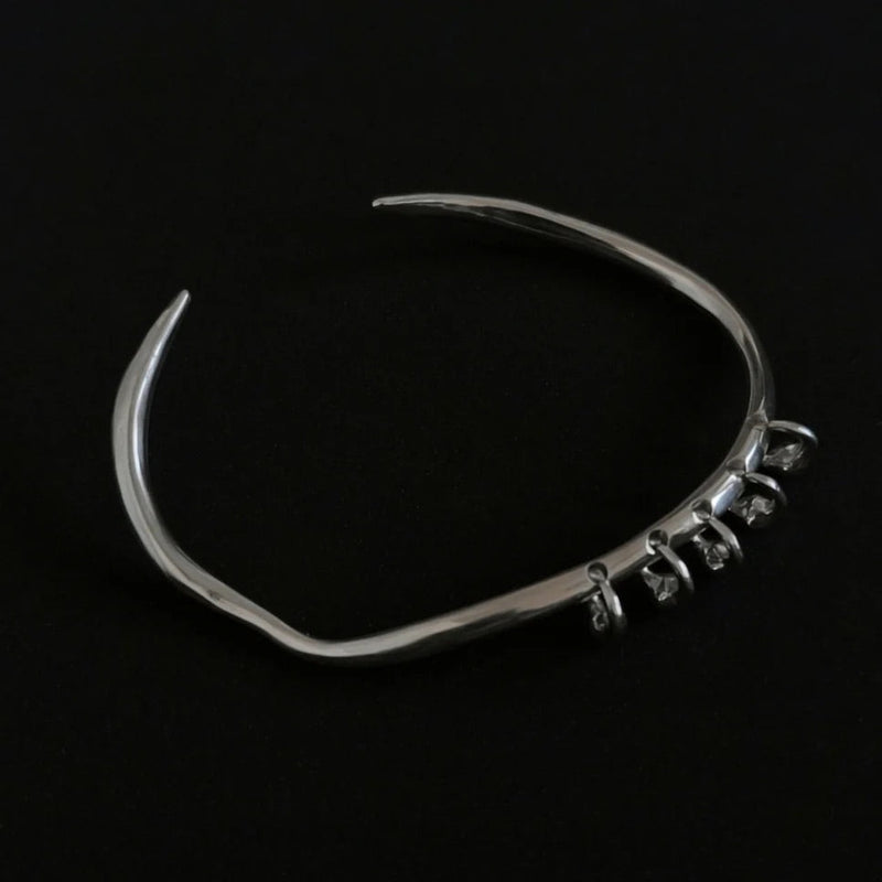 One-of-a-kind silver bangle featuring an organic, asymmetrical shape with delicate dangling accents for a modern, minimalist edge.