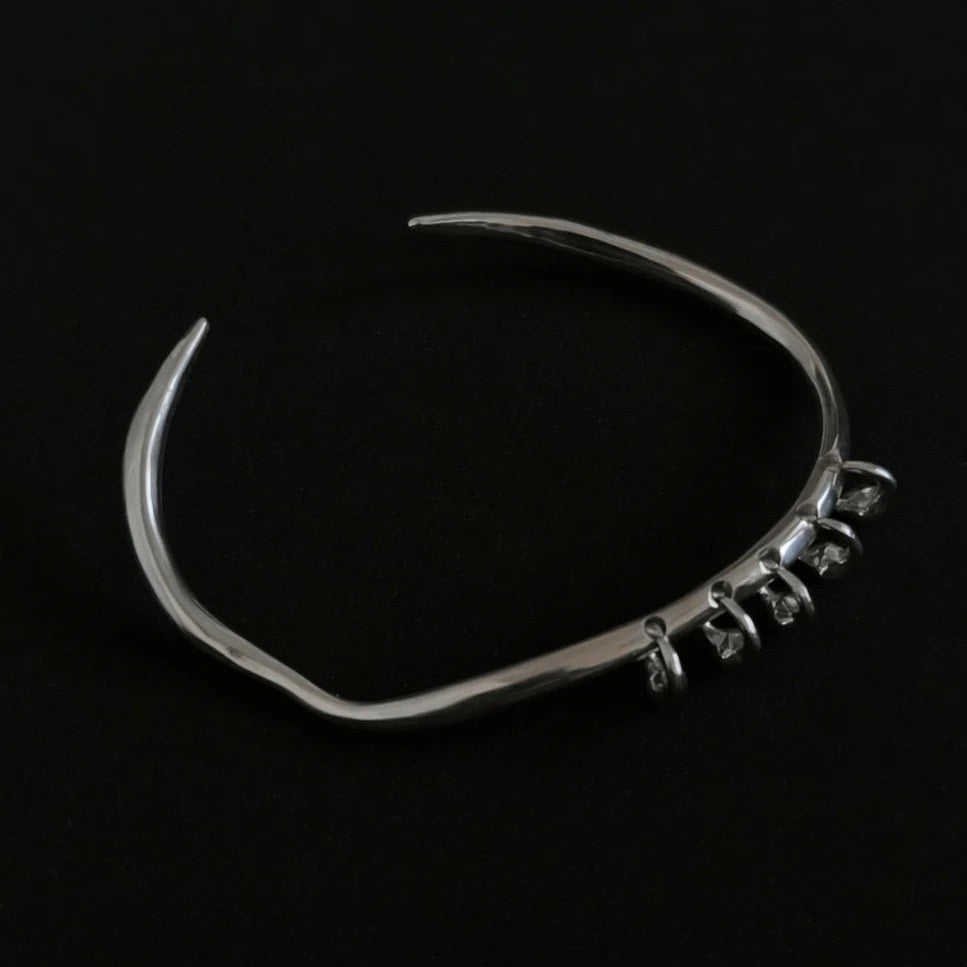 One-of-a-kind silver bangle featuring an organic, asymmetrical shape with delicate dangling accents for a modern, minimalist edge.
