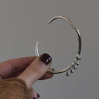 One-of-a-kind silver bangle featuring an organic, asymmetrical shape with delicate dangling accents for a modern, minimalist edge.