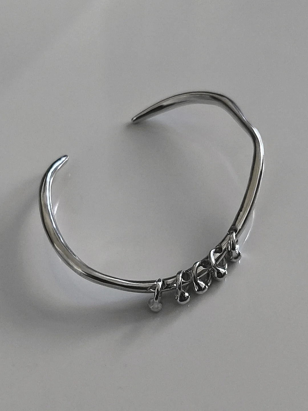 One-of-a-kind silver bangle featuring an organic, asymmetrical shape with delicate dangling accents for a modern, minimalist edge.