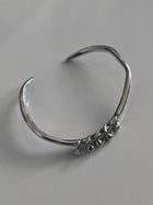One-of-a-kind silver bangle featuring an organic, asymmetrical shape with delicate dangling accents for a modern, minimalist edge.