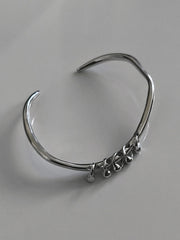 One-of-a-kind silver bangle featuring an organic, asymmetrical shape with delicate dangling accents for a modern, minimalist edge.