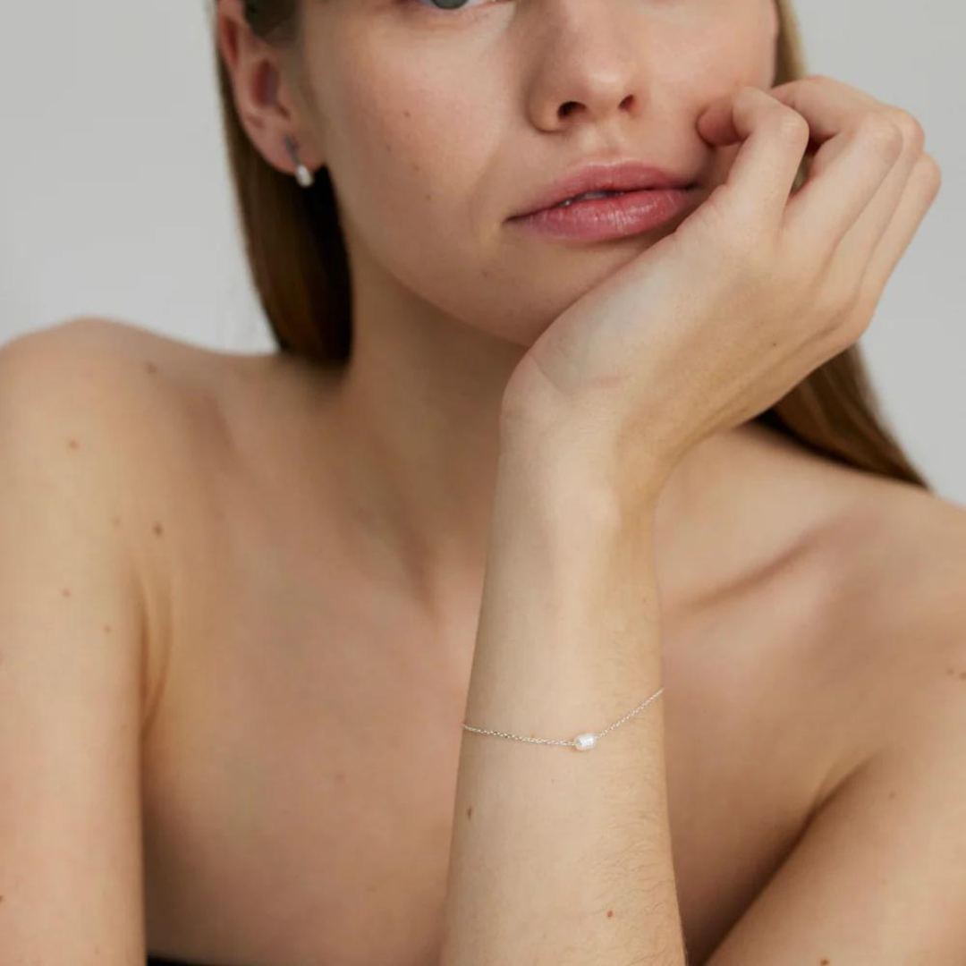A woman wearing a silver bracelet with a freshwater pearl on their wrist.