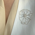 Close-up of a person wearing a white garment with a decorative floral brooch.