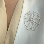 Close-up of a person wearing a white garment with a decorative floral brooch.