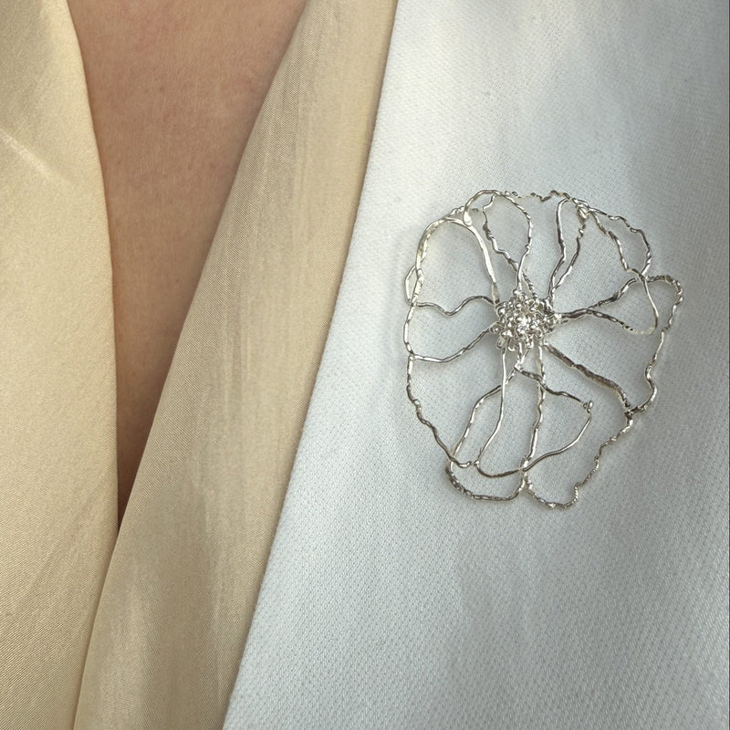 Close-up of a person wearing a white garment with a decorative floral brooch.