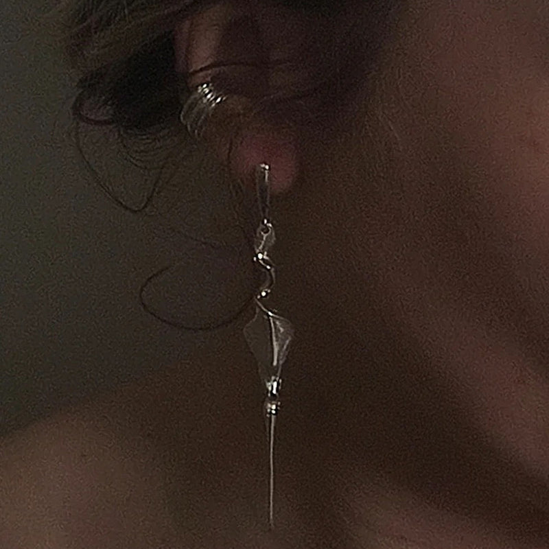 A close-up of a person's ear wearing a long, dangling silver earring with a faceted bead and a small silver hoop earring in the ear cartilage.