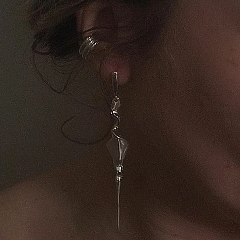A close-up of a person's ear wearing a long, dangling silver earring with a faceted bead and a small silver hoop earring in the ear cartilage.