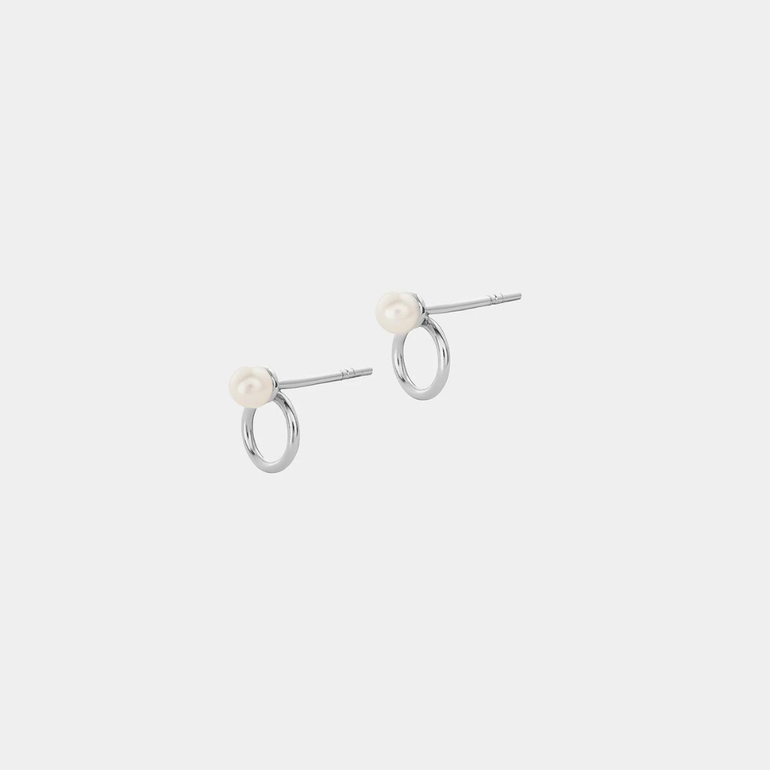 A pair of silver earrings featuring a round pearl attached to a silver ring, presented on a white background.