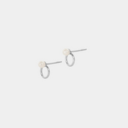 A pair of silver earrings featuring a round pearl attached to a silver ring, presented on a white background.