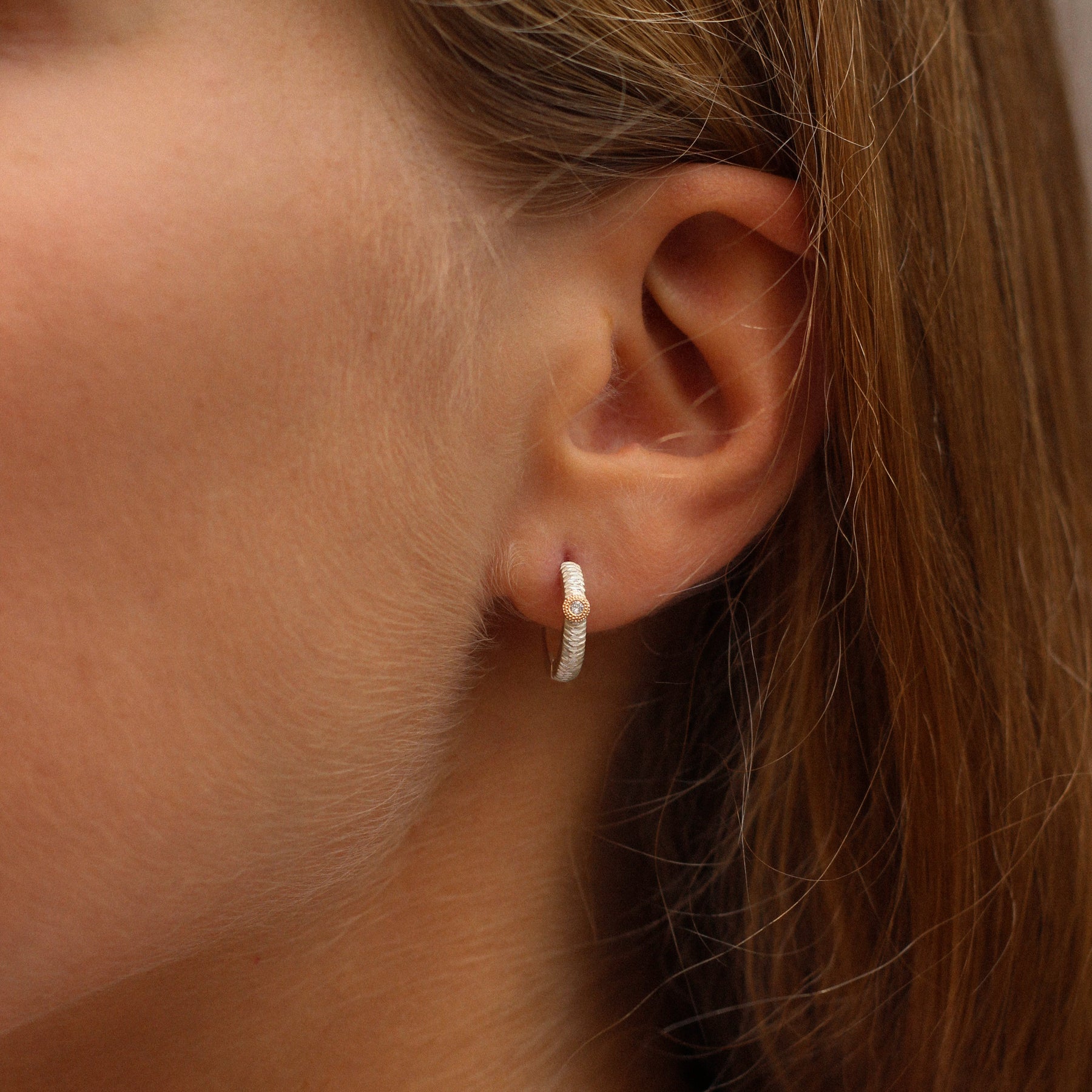 Close-up of an ear wearing a small hoop earring with a gemstone