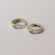 Pair of silver hoop earrings with emeralds on a light gray background