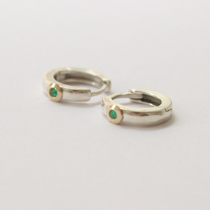 Two silver rings with emeralds on a light gray background