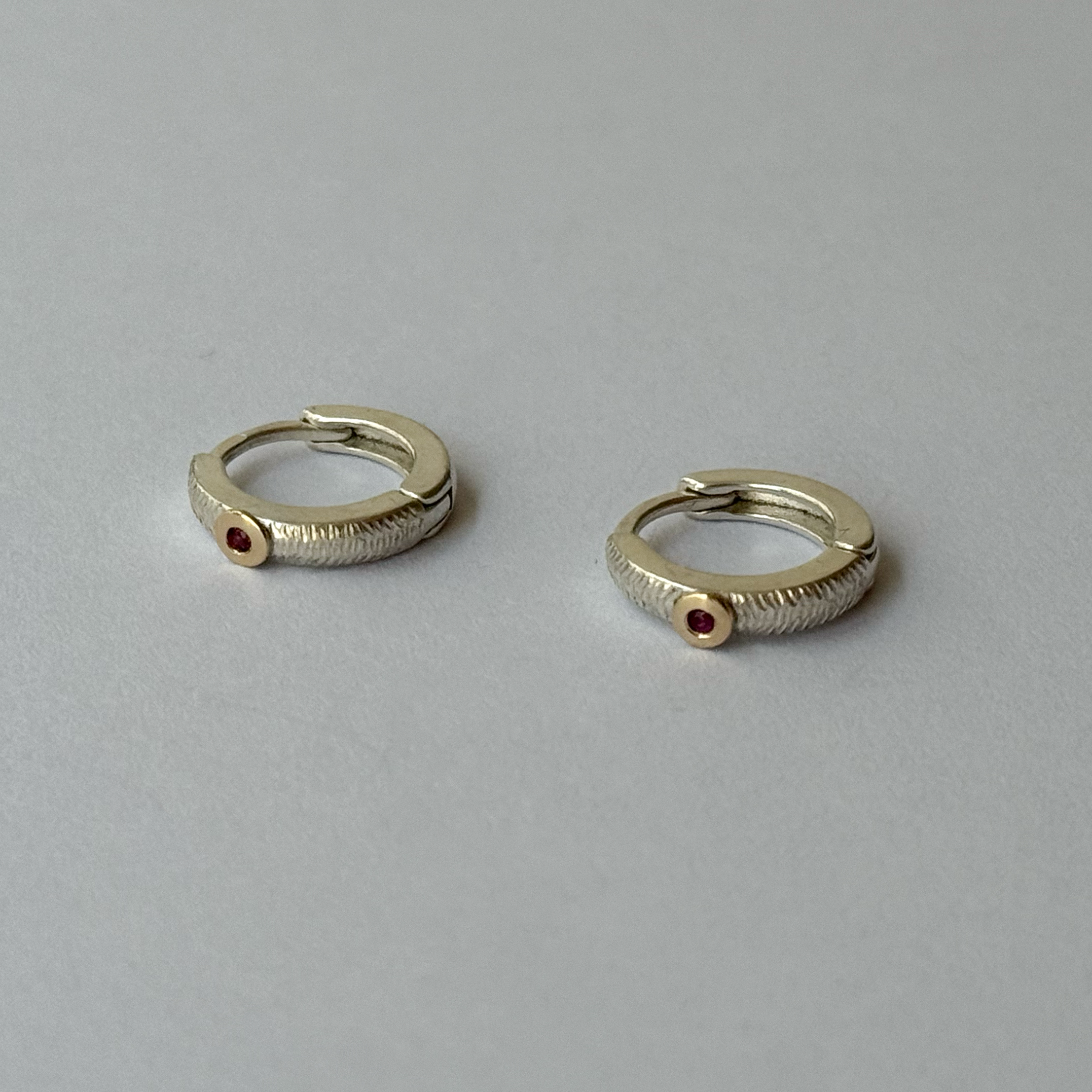 A pair of silver hoop earrings with small rubies attached to them, set against a light background.