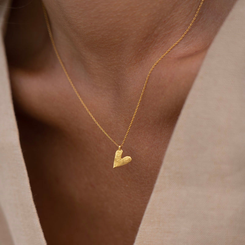 A gold plated silver necklace with a heart-shaped pendant, worn by a person with a light skin tone, presented in a close-up shot focusing on the necklace.