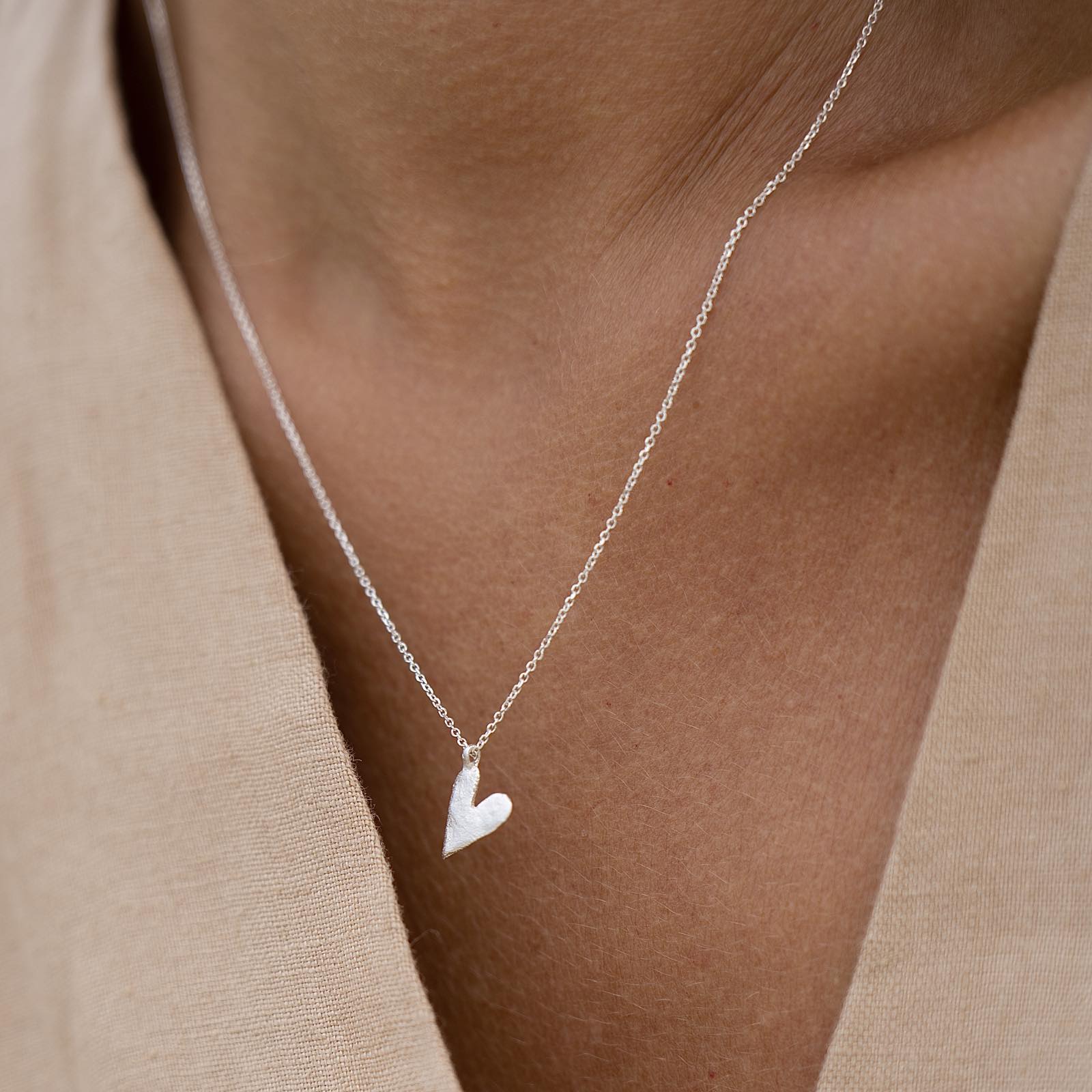 A heart-shaped silver necklace on a person's neck, presented as a gift in a designer-stamped box.