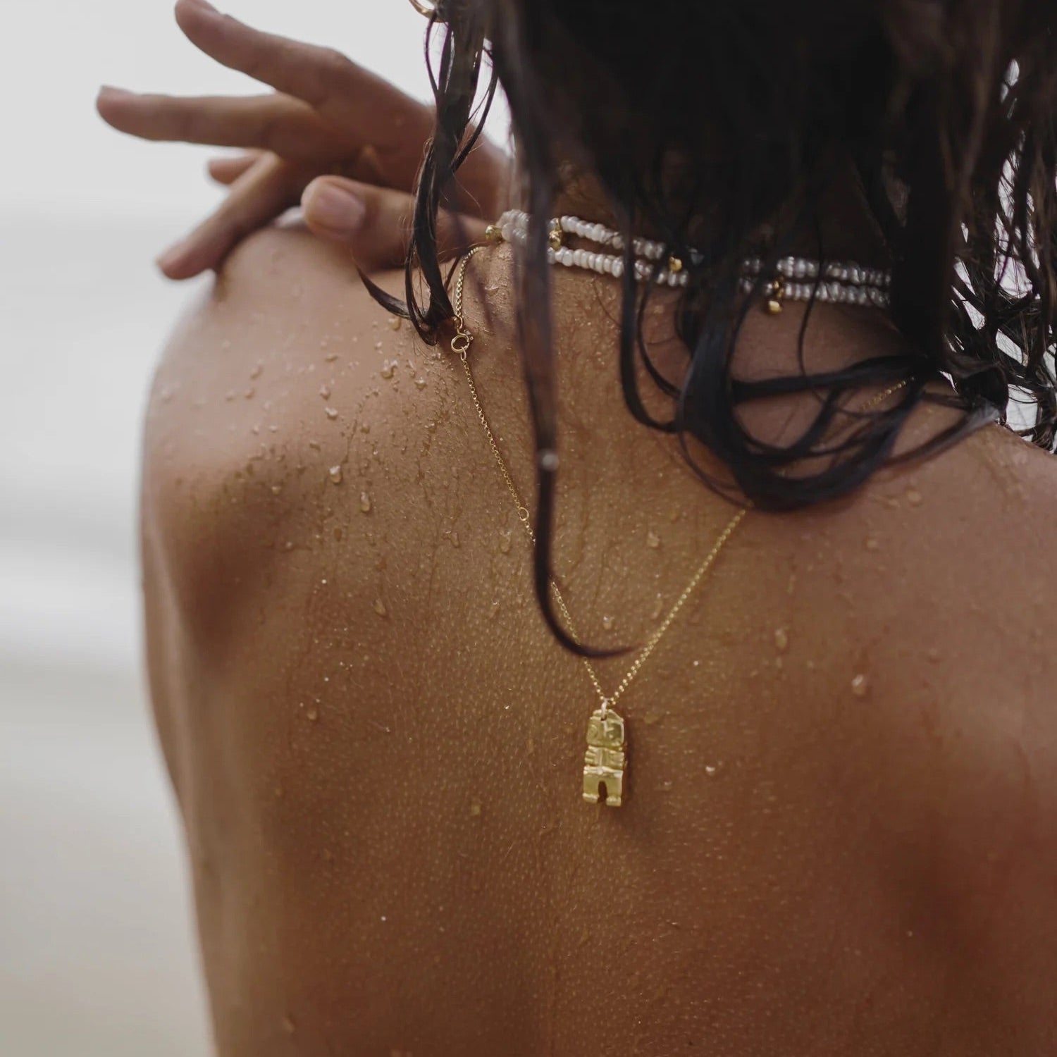 Close-up of a person wearing a gold necklace with a pendant, with water droplets on their skin.