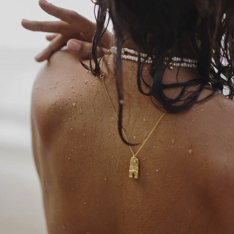 Close-up of a person wearing a gold necklace with a pendant, with water droplets on their skin.