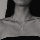 Close-up of a person wearing a necklace with a moon pendant.