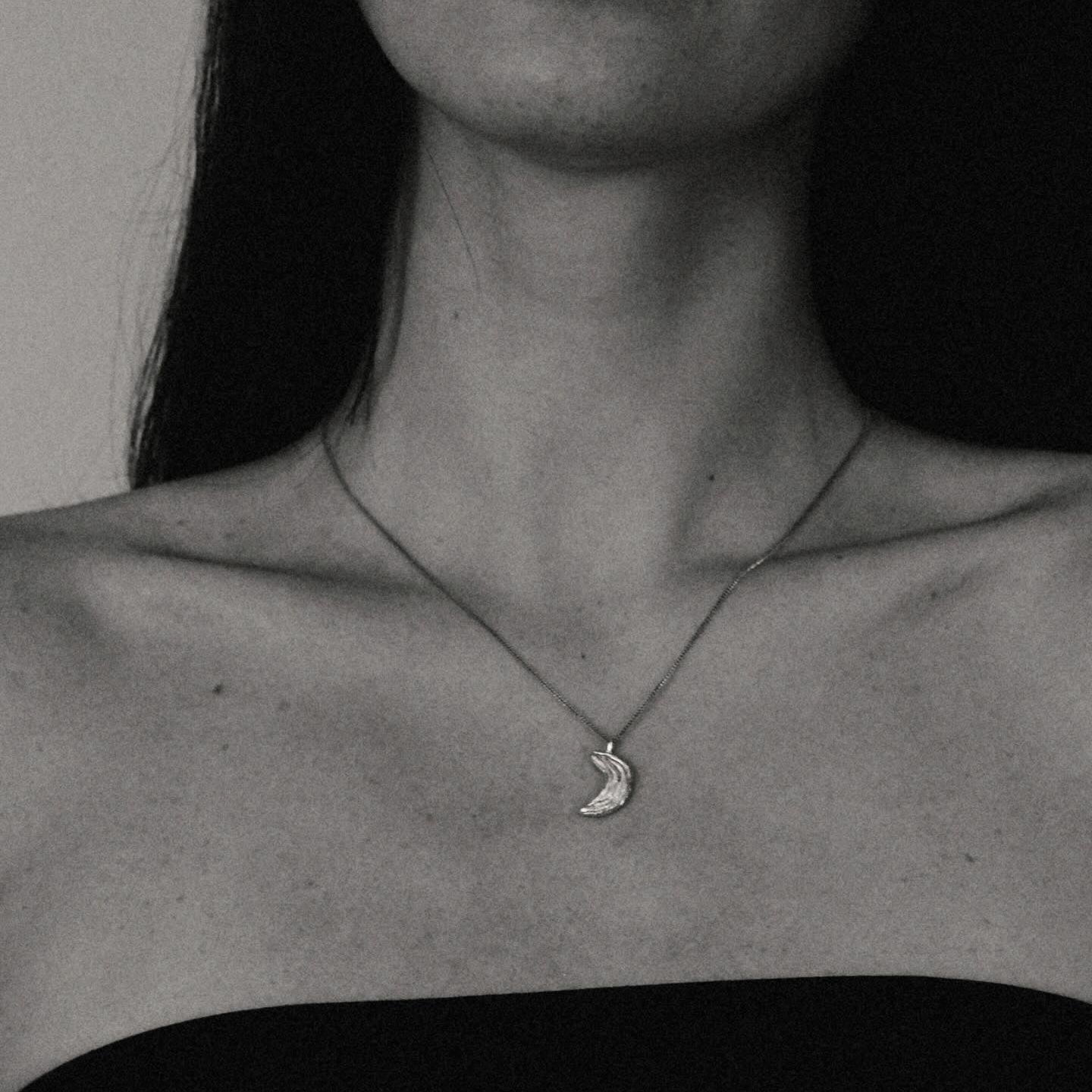 Close-up of a person wearing a necklace with a moon pendant.