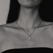 Close-up of a person wearing a necklace with a moon pendant.