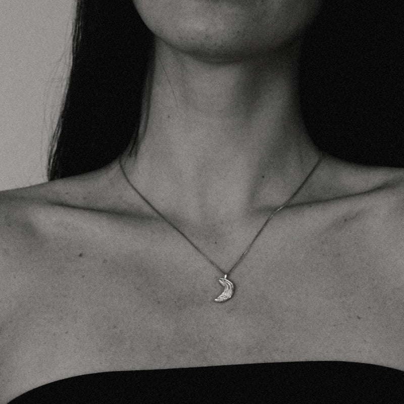 Close-up of a person wearing a necklace with a moon pendant.