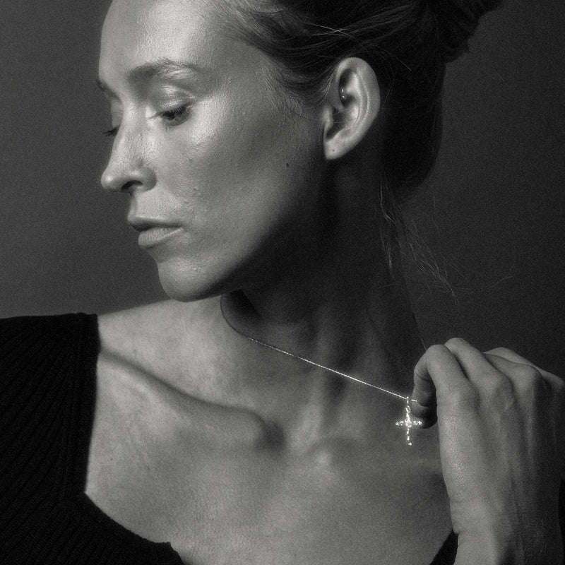 Black and white close-up of a woman adjusting a necklace with a cross pendant.