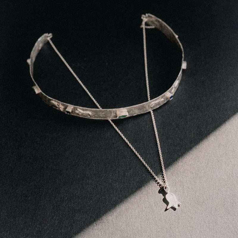 Silver choker necklace with a pendant on a dark surface