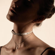 Close-up of a person wearing a silver necklace with a plain background