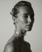 Black and white portrait of a woman wearing a delicate necklace against a plain background